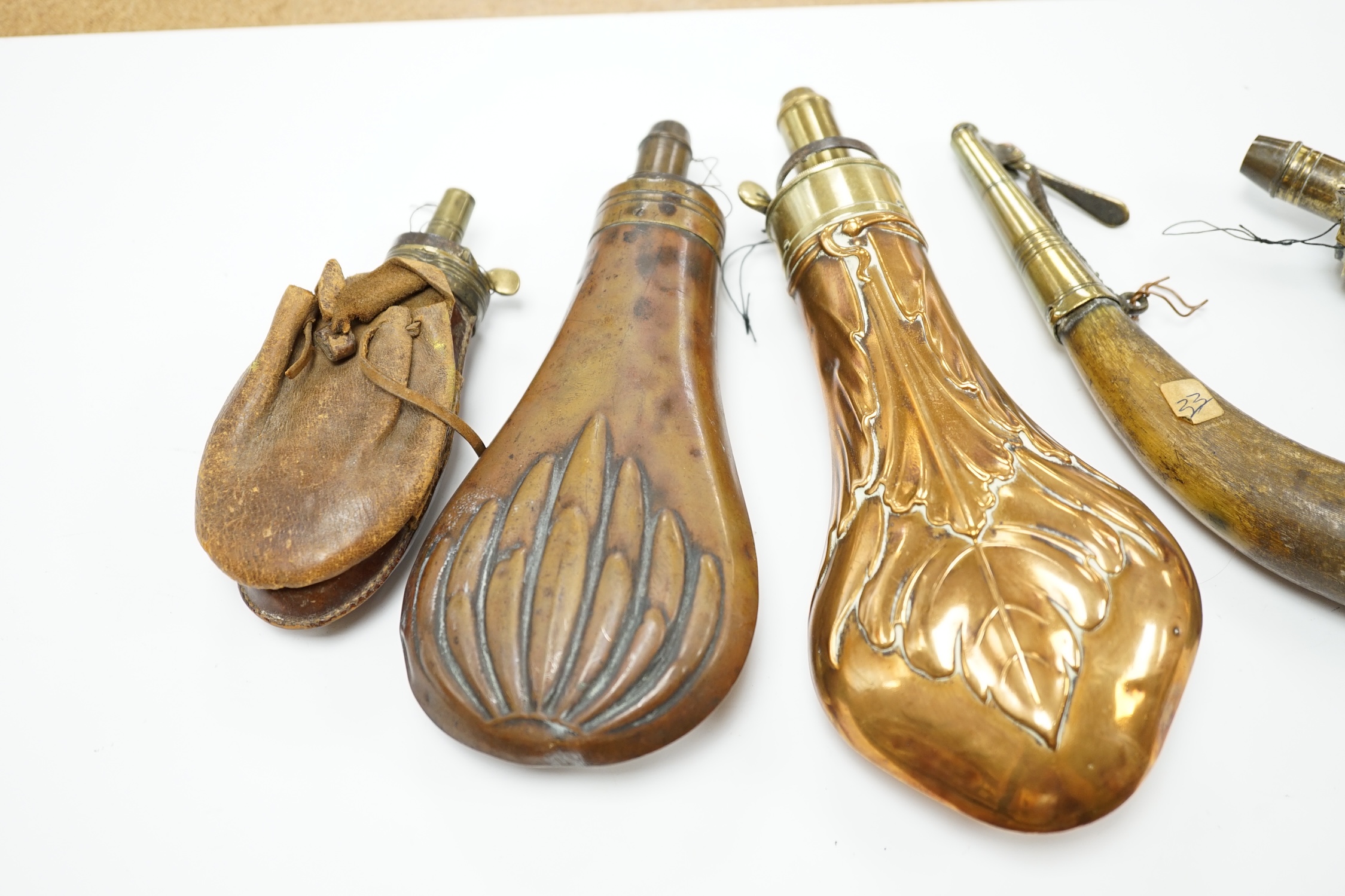 Five 19th century powder flasks; three copper and brass flasks, two with embossed decoration to the bodies, a leather covered flask and a horn Royal Artillery priming horn. Condition - poor to fair